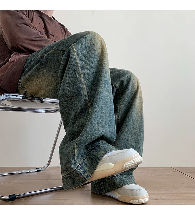 Person wearing distressed wide leg jeans sitting on a metal chair with white sneakers
