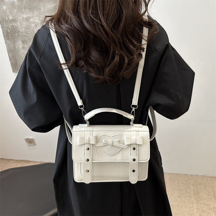 Elegant small PU leather bag in white with heart and bow details worn on back
