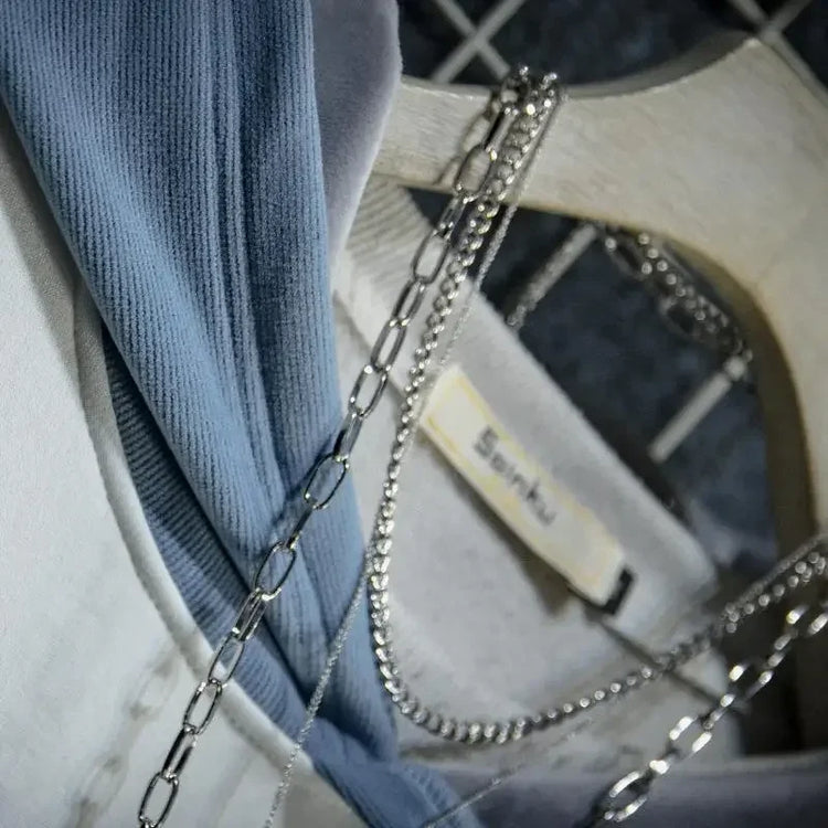 Close-up of cute cat anime hoodie fabric in blue and gray with silver chain necklace hanging on wooden hanger