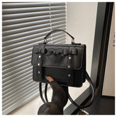 Elegant small PU leather bag in black with bow detail and top handle held near window blinds