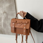 Elegant small PU leather bag in brown with decorative bow and heart detail held by hand