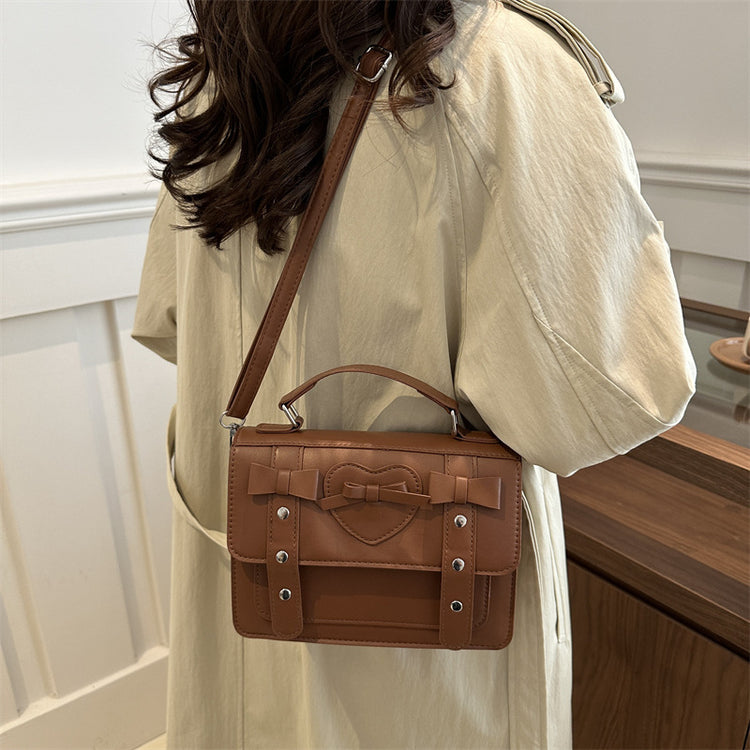 Elegant small PU leather bag in brown with heart and bow design worn by a woman in beige coat