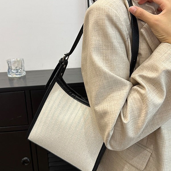 Elegant stitched handbag for women in cream and black worn over beige blazer sleeve